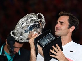 Switzerland's Roger Federer cries as he holds the winner's trophy after beating Croatia's Marin Cilic (L) in their men's singles final match on day 14 of the Australian Open tennis tournament in Melbourne on Jan. 28, 2018.