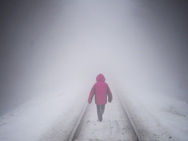 A young girl walks along a snow covered train track during heavy fog in a small town west of Montreal, Friday, January 12, 2018.