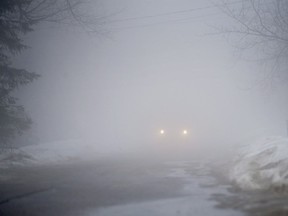 A motorist makes their way down a street during heavy fog.