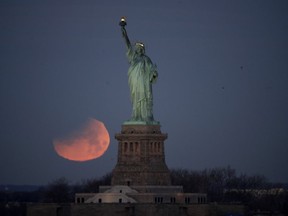 The Statue of Liberty is backdropped by a supermoon, Wednesday, Jan. 31, 2018, seen from the Brooklyn borough of New York. The supermoon, which is the final of three consecutive supermoons, also experience lunar eclipse as it set over the horizon, but only a partial eclipse was visible in the East Coast.