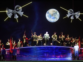Jack Kennedy (Matthew Worth) on the moon with Nikita Khrushchev (Colin Judson) and chorus in the opera JFK, from Opéra de Montréal. The Earth shines above the cast.
