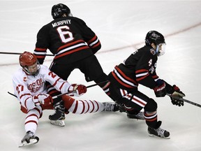 Boston University forward Brady Tkachuk (27) is knocked to the ice by Northeastern defenseman Collin Murphy (6) as defenseman Jeremy Davies, right, skates away with the puck during the third period of the championship game of the Beanpot hockey tournament in Boston, Monday, Feb. 12, 2018.