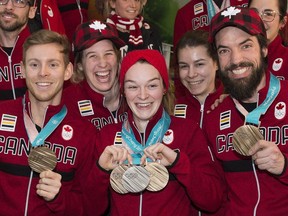 Kim Boutin, centre, and Pascal Dion, left, and Charles Hamelin, right, show off their Pyeongchang 2018 Olympic Winter medals with fellow teammates on their arrival back from the games at Trudeau airport on Monday.