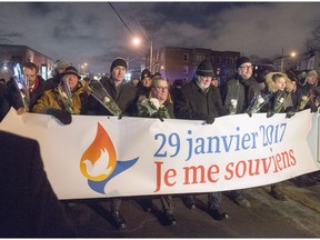 Prime Minister Justin Trudeau, middle left to right, Quebec City mayor Regis Labeaume and Quebec Premier Philippe Couillard march with a banner during a vigil to commemorate the one-year anniversary of the Quebec City mosque shooting in Quebec City, Monday, Jan. 29, 2018.