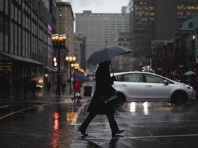 A man crosses the street with an umbrella at the intersection of McGill College Ave. and de Maisonneuve Blvd.
