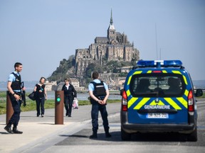 People stand on the road leading to the Mont-Saint-Michel as Gendarmes block the access after it was evacuated on April 22, 2018 of its tourists and residents "as a precautious measure" after an unidentified suspect allegedly threatened to attack law enforcement members.