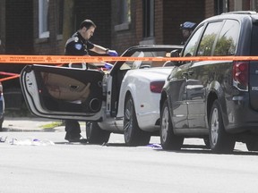 A Montreal police officer gathers evidence from a Bentley ragtop, where the driver was shot at the corner of Garnier and Bélanger on Monday May 14, 2018.