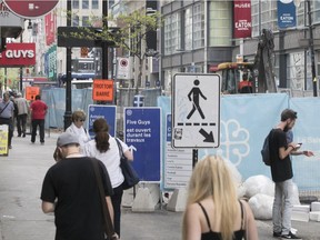 Pedestrians walk on the sidewalk of Ste-Catherine St. near Robert-Bourassa Blvd., while work crews work on other side of barrier on Friday May 25, 2018.