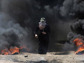 A Palestinian woman walks through black smoke from burning tires during a protest on the Gaza's border with Israel, May 14, 2018.
