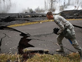 U.S. Air National Guardsman John Linzmeier looks at cracks as toxic gases rise near by in the Leilani Estates subdivision near Pahoa, Hawaii Friday, May 18, 2018. Hawaii residents covered their faces with masks after a volcano menacing the Big Island for weeks exploded, sending a mixture of pulverized rock, glass and crystal into the air in its strongest eruption of sandlike ash in days.