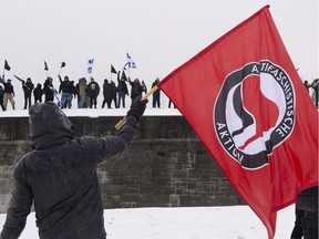 An anti-fascist demonstrator waves a flag toward members of the extreme-right group Atalante, standing on the fortified walls of Old Quebec, during a clash between the two sides in Quebec City on Nov. 25, 2017.