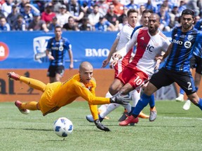Montreal Impact goalkeeper Evan Bush makes a save on a shot by New England Revolution forward Teal Bunbury, centre, as Impact defender Victor Cabrera looks on during first half MLS action Saturday, May 5, 2018 in Montreal.