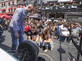 Canadian Paralympic swimmer Benoit Huot left, and Olympic diver Roseline Filion, right, get instructions on how to change an F1 tire before competing during Grand Prix festivities on Crescent St. in Montreal, on Thursday, June 7, 2018.
