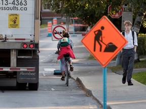 A cyclist tries to find room to ride between road signs and a large truck near the Montreal West train station in Montreal on Wednesday September 13, 2017.