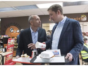 Conservative Leader Andrew Scheer, right, and Chicoutimi-Le Fjord candidate Richard Martel chat as they carry food at the famous Boivin cheese counter, Thursday, June 14, 2018 in Saguenay, Que.