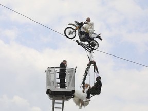 Pastor Stefan Gierung, left, stands in a cage atop of a fire service ladder in front of bride Nicole Backhaus, center, and groom Jens Knorr, right, both sitting in a swing dangling under a motorcycle with artist Falko Traber, top, during the wedding ceremony atop a tightrope in Stassfurt, Germany, Saturday, June 16, 2018. (Peter Gercke/dpa via AP) ORG XMIT: DMSC123