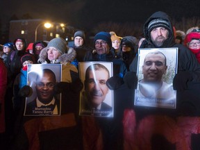 People hold pictures of the victims at a vigil to commemorate the one-year anniversary of the Quebec City mosque shooting, in Quebec City, Monday, Jan. 29, 2018.