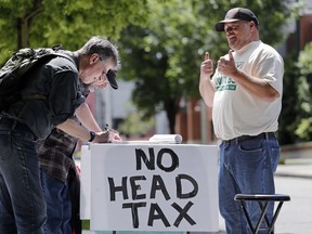 In this May 24, 2018, photo, paid signature gatherer John Ellard, right, gives thumbs-up as two men stop to sign petitions to put on the November ballot a referendum on Seattle's head tax, in Seattle.