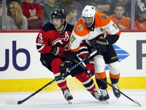 New Jersey Devils' Adam Henrique, left, and Philadelphia Flyers' Wayne Simmonds, cross sticks as they move towards the action during the second period of an NHL hockey game, Saturday, Jan. 21, 2017, in Philadelphia.