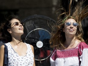 Julia Lopez Ramos and her sister Paula, right, cool down in front of a large fan that is equipped with a water misting ring as Montreal endures a heat wave in Montreal on Tuesday July 3, 2018.