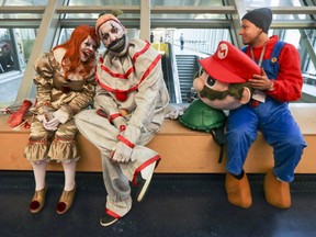 Marie-Claude Latour, dressed as Pennywise, left, sits with Gaetan Dubois, dressed as Twisty, as Yannick L'Abbe prepares to put on his Mario head at Montreal Comiccon at the Palais des congrès Friday July 6, 2018.