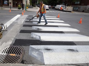 A city worker puts the finishing touches on a freshly painted 3D crosswalk in the Outremont borough of Montreal on July 10, 2018.