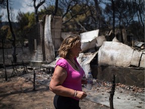 A woman walks in front of her burnt house following a wildfire at the village of Neos Voutzas, near Athens, on July 25, 2018.