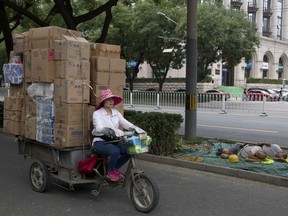 A woman transports goods past workers sleeping on a street-side in Beijing Tuesday, July 10, 2018. The Trump administration is readying tariffs on another $200 billion in Chinese imports, ranging from burglar alarms to mackerel, escalating a trade war between the world’s two biggest economies.