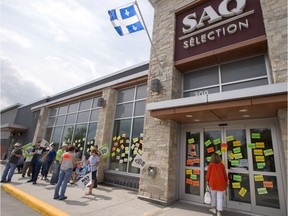 A customer looks through the windows as liquor store employees walk the picket line in front of an SAQ outlet, July 17, 2018 in Rosemère.