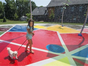 Gracie Lepage, 6, cools off with one of her dogs at the new splash pad on Paul-Gerin-Lajoie Street near St-Charles Ave. in Vaudreuil-Dorion on Sunday.