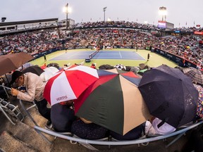 Tennis fans huddle under umbrellas as Simona Halep plays Anastasia Pavlyuchenkova Wednesday evening. The weather forced the postponement of four matches.