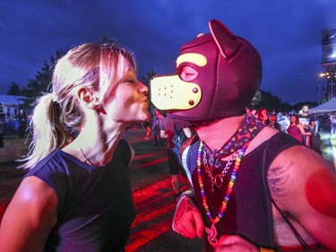 Catherine Servedio kisses Joey Lachapelle on the snout of his dog mask during Pride festivities in Montreal on Friday, August 17, 2018.