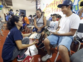 Volunteer Aura Perez, left, brings shoes to Carlos Del Valle, right, with his brother Rodrigo and mother Ann Lesly Altamirano at the Welcome Hall Mission on Aug. 14, 2018.