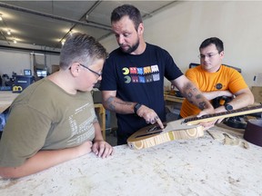 James Klym talks to son Trevor and co-director Romain Huon, right, about a guitar he made out of 20 skateboards at Helios Makerspace. Klym not only teaches guitar-making but also gives courses on playing the instrument.