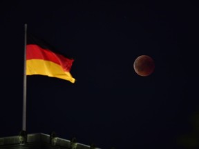 The total lunar eclipse is picutred next to the German national flag atop the Reichstag building, seat of the German lower house of parliament Bundestag in Berlin on July 27, 2018. The longest "blood moon" eclipse this century began on July 27, coinciding with Mars' closest approach in 15 years to treat skygazers across the globe to a thrilling celestial spectacle.