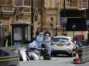Forensics officers work near the car that crashed into security barriers outside the Houses of Parliament in London, Tuesday, Aug. 14, 2018. Authorities said in a statement Tuesday that a man in his 20s was arrested on suspicion of terrorist offenses after a silver Ford Fiesta collided with a number of cyclists and pedestrians before crashing into the barriers during the morning rush hour.