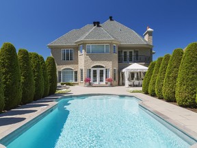 Two rows of perfectly trimmed cedar trees add an air of grandeur to the swimming pool in the lavish backyard.