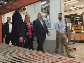 Quebec Liberal leader Philippe Couillard, his wife Suzanne Pilote and local candidate Simon Laboissonnière, right, walk the corridors of a Bombardier plant in La Pocatière on Aug. 29, 2018.