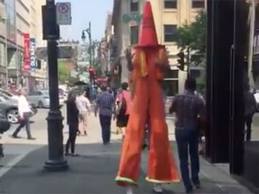 A man on stilts with a traffic cone on his head in downtown Montreal