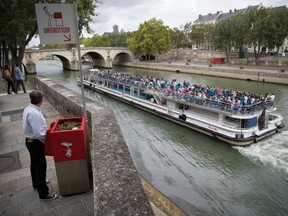 A man stands at a "uritrottoir" public urinal on August 13, 2018, on the Saint-Louis island in Paris, as a "bateau mouche" tourist barge cruises past. - The city of Paris has begun testing "uritrottoirs", dry public urinals intended to be ecological and odorless, but that make some residents cringe.