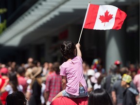 A young girl waves a Canadian flag while being carried through the crowd during Canada Day celebrations in Vancouver, B.C., on Saturday, July 1, 2017.