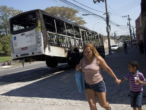 A woman and a boy walk past a bus allegedly set on fire by drug traffickers in the Bonsucesso neighborhood, Rio de Janeiro, Brazil, Monday, Aug. 20, 2018. Since February, the military has been in charge of security in the state of Rio de Janeiro, which is struggling to curb a spike in violence.