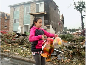 Nine-year-old Emna Ben-Salem carries out some of the toys she could find in her bedroom of her family's home (rear), which will more than likely be demolished as half the roof and side on the triplex was ripped off in the tornado.