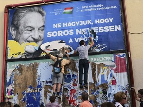 FILE -- In this Wednesday, July 12, 2017 photo activists of the Egyutt (Together) party tear down an ad by the Hungarian government against George Soros, in Budapest, Hungary. The Open Society Foundations, created by billionaire philanthropist George Soros, says it has filed applications before the European Court of Human Rights and Hungary's Constitutional Court about recent laws in Hungary targeting civic groups working with refugees and asylum-seekers.
