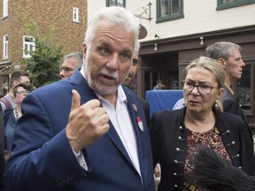 Quebec Liberal Leader Philippe Couillard speaks to reporters while visiting the site of the Fête Arc-en-Ciel for LGBTQ, Saturday, Sept. 1, 2018, in Quebec City. Couillard's wife, Suzanne Pilote, right, looks on.