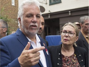 Quebec Liberal Leader Philippe Couillard speaks to reporters while visiting the site of the Fête Arc-en-Ciel for LGBTQ, Saturday, Sept. 1, 2018, in Quebec City. Couillard's wife, Suzanne Pilote, right, looks on.