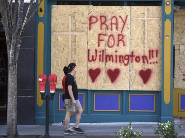 People walk by the boarded up front windows of Bourbon St. in preparation for Hurricane Florence in Wilmington, N.C., Sept. 12, 2018.