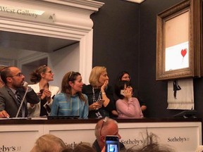 The spray-painted canvas “Girl With Balloon” went under the hammer at Sotheby’s in London, fetching more than three times its pre-sale estimate and equaling a record price for the artist.
Then, as an alarm sounded, it ran through a shredder embedded in the frame, leaving half the canvas hanging from the bottom in strips.