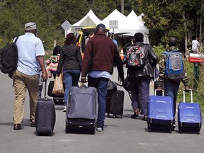 A family from Haiti approaches a tent in St-Bernard-de-Lacolle as they haul their luggage down Roxham Rd. in Champlain, N.Y., Monday, Aug. 7, 2017.