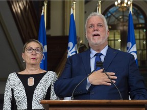 Quebec Premier and Liberal Leader Philippe Couillard touches his heart while members of his staff applaud as announces his resignation as Premier and MNA for the riding of Roberval, Thursday, October 4, 2018 at the legislature in Quebec City. Couillard's wife Suzanne Pilote, left, looks on.